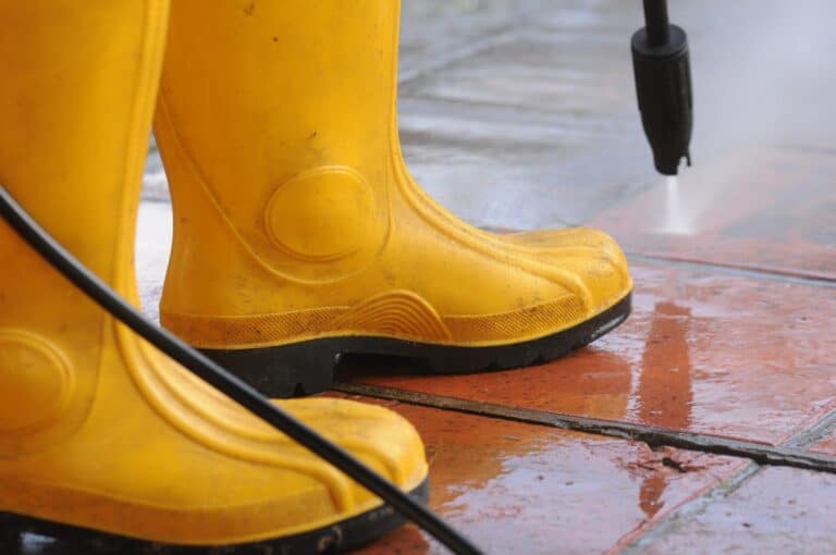 A person wearing yellow rubber boots with high-pressure water nozzle cleaning the dirt in the tiles