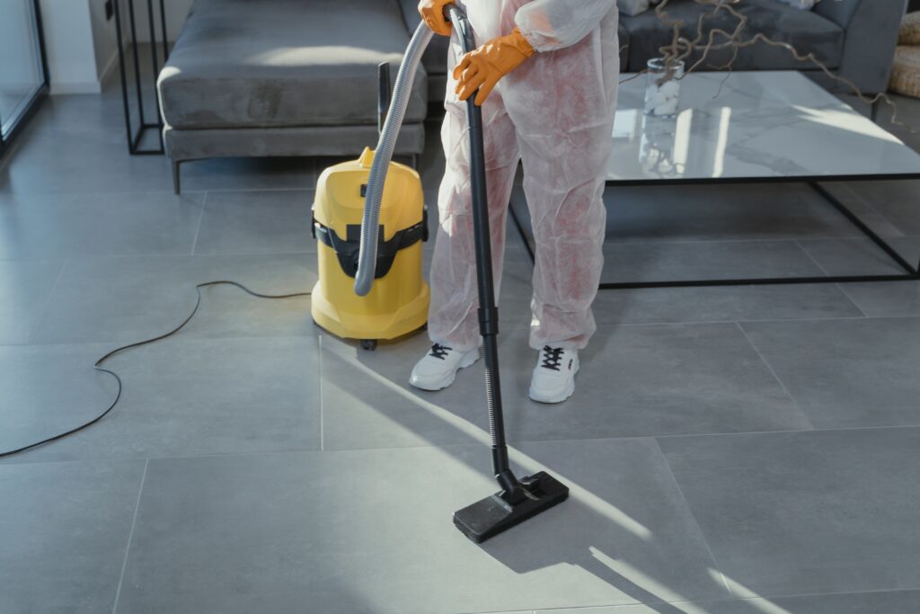 Woman in pink pants and white sneakers cleaning the floor with professional cleaning vcuum